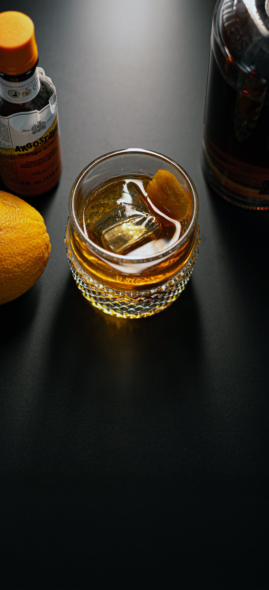 Rocks Glass holding an amber cocktail with a large ice cube and orange peel